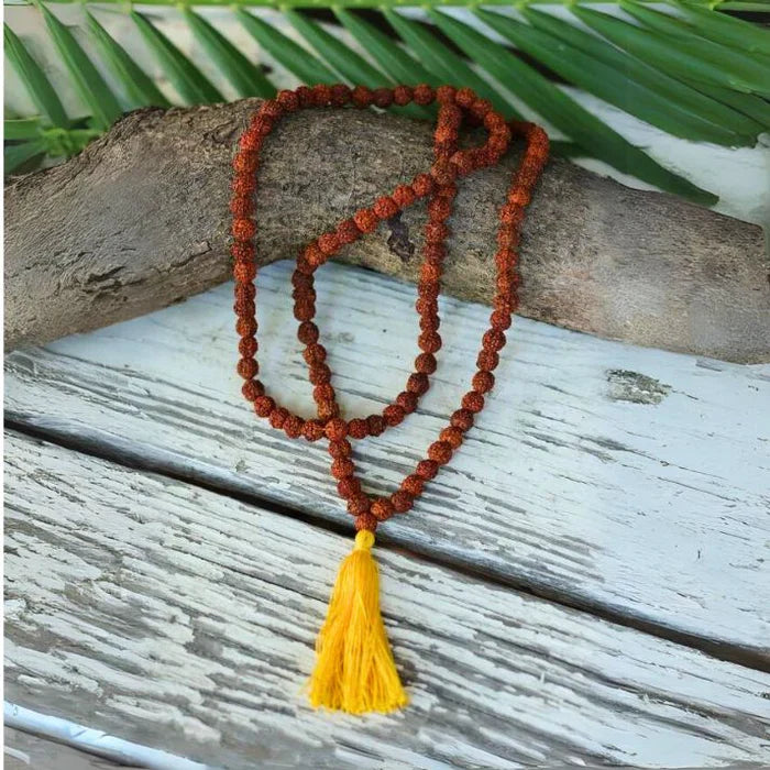Rudraksha Jaap Mala with a yellow tassel displayed on a rustic wooden background