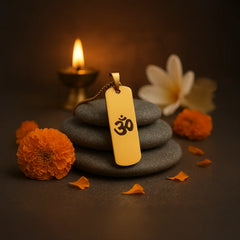24K gold OM necklace on smooth stones surrounded by marigold flowers and a warm candlelight